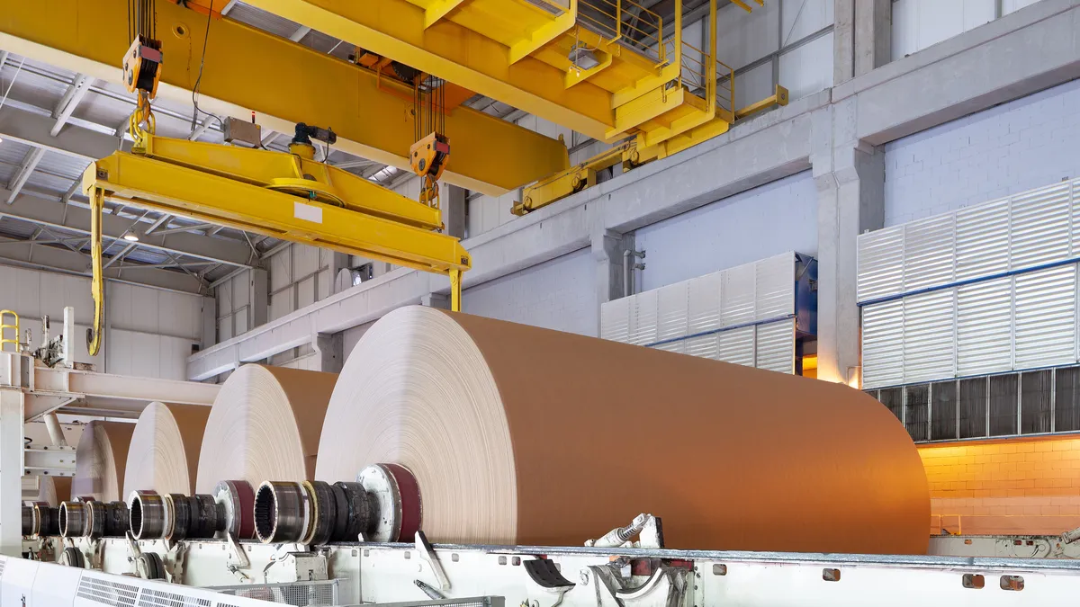 Paper mill interior with yellow gantry crane above large white paper rolls