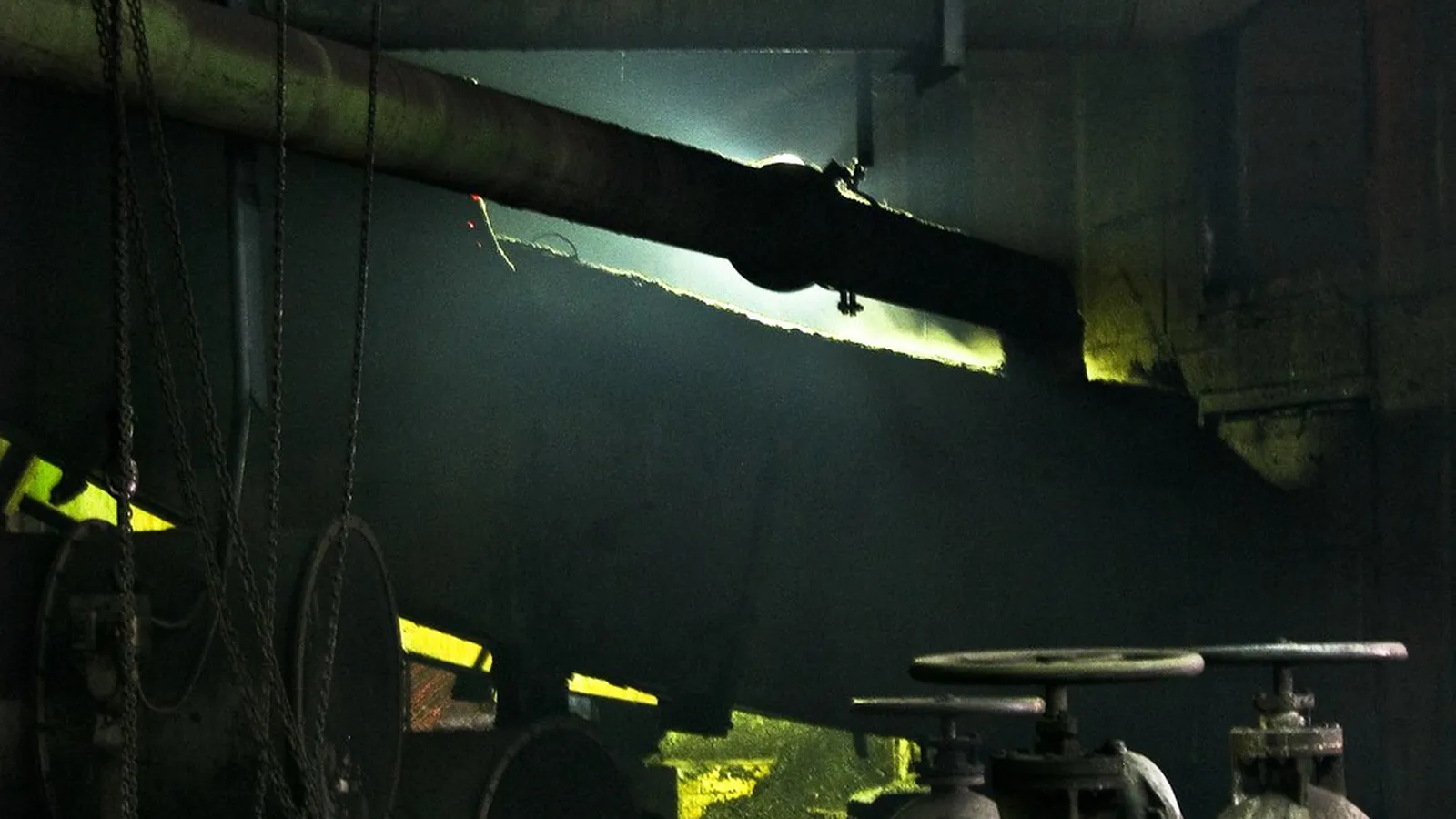 Insulated steam main with green valve handwheels lit in a dark plant room